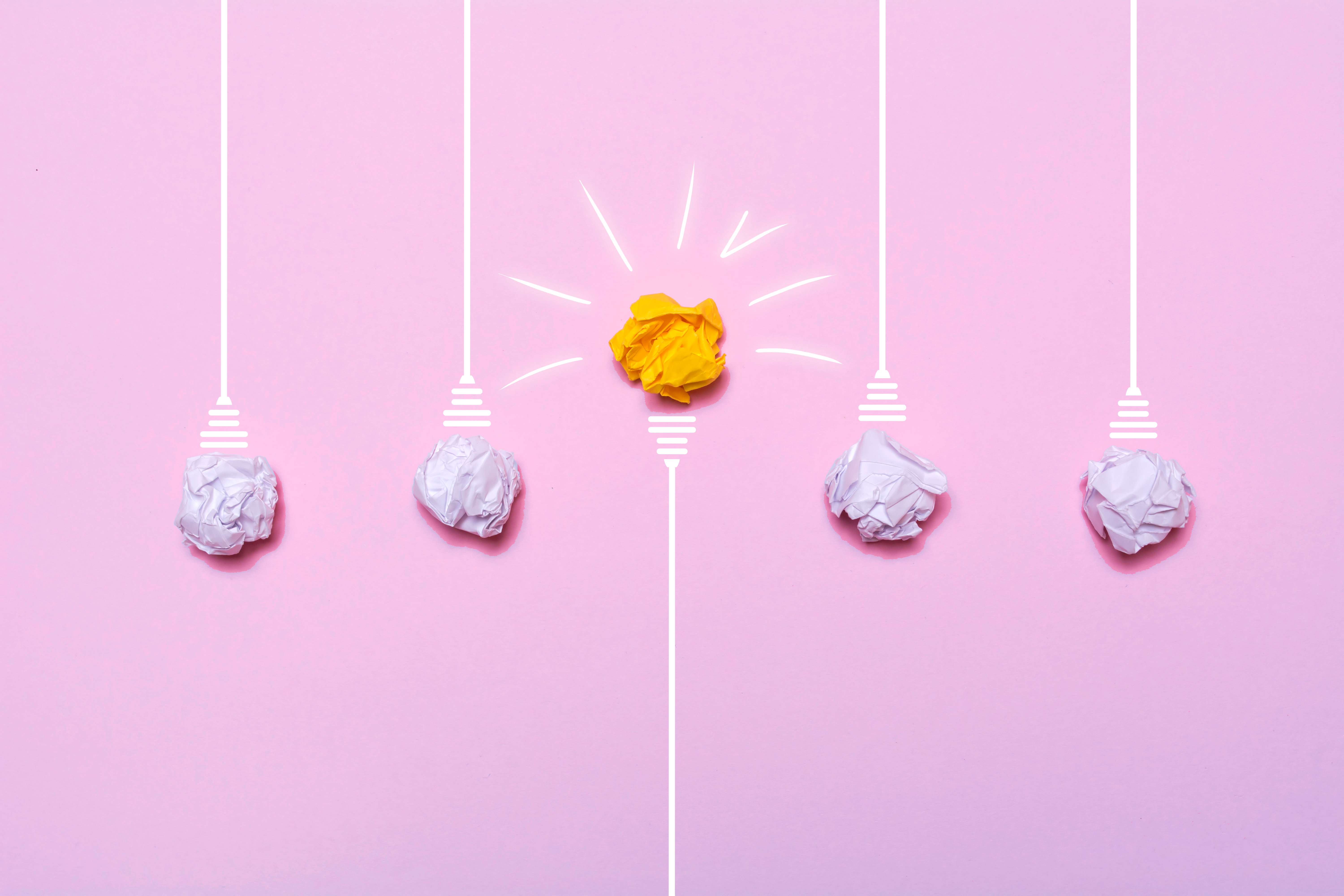 una metáfora visual de la creatividad en las que las bombillas son bolas de papel arrugado de color blanco y hay una en medio que parece encendida de color amarillo